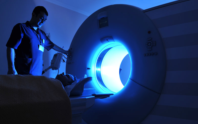 A medical operative oversees a person about to enter the inside of a large scanner