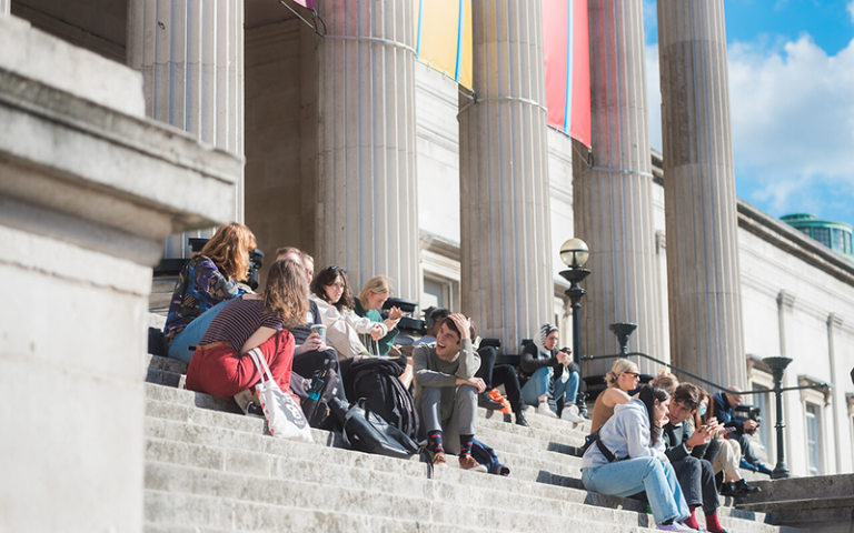  students sitting on the steps of the UCL Portico building