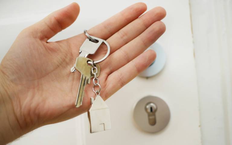 A hand holding a bunch of keys, in front of a white front door with the handle and lock visible