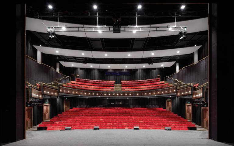Image of the red velvet seats in the Bloomsbury Theatre, seen from the stage with stage lights illuminated