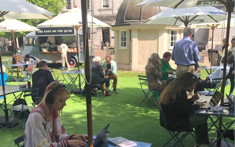 The Café on the Quad, with a food van and outdoor tables shaded by umbrellas where people are eating and working