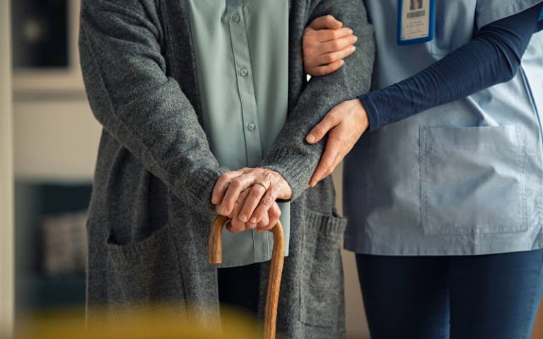 A nurse helps an elderly patient to walk with a cane
