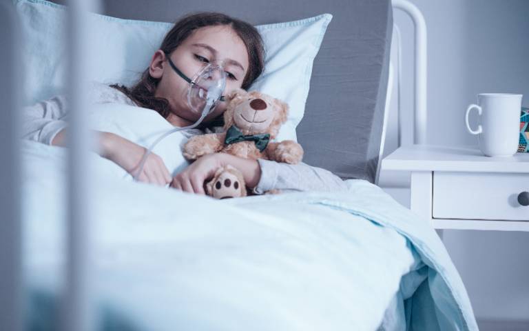 child wearing an oxygen mask in a hospital bed