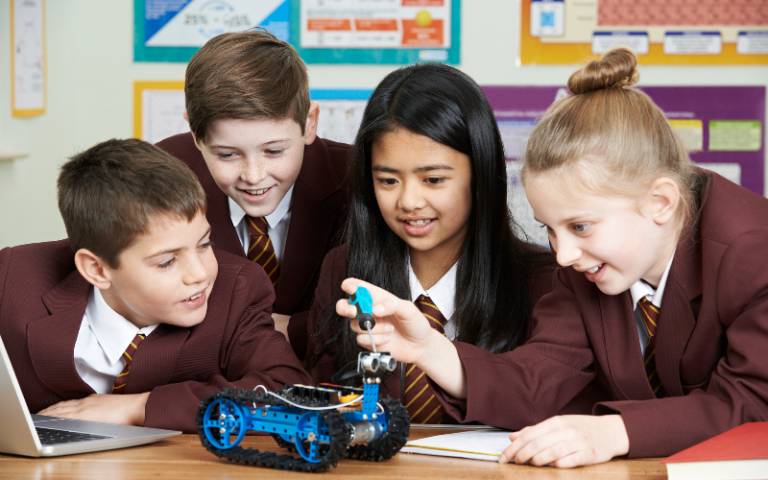 Four children tinker with a small robot in a classroom
