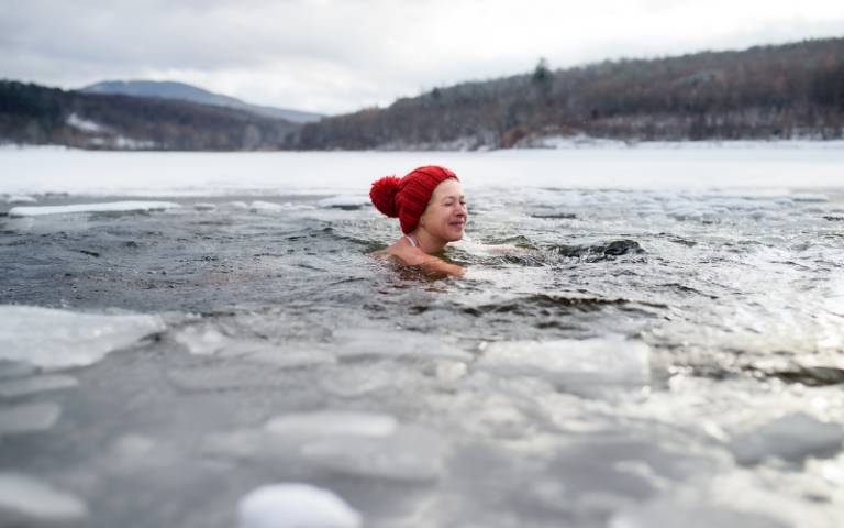 A happy active senior woman in hat diving outdoors in water in winter,