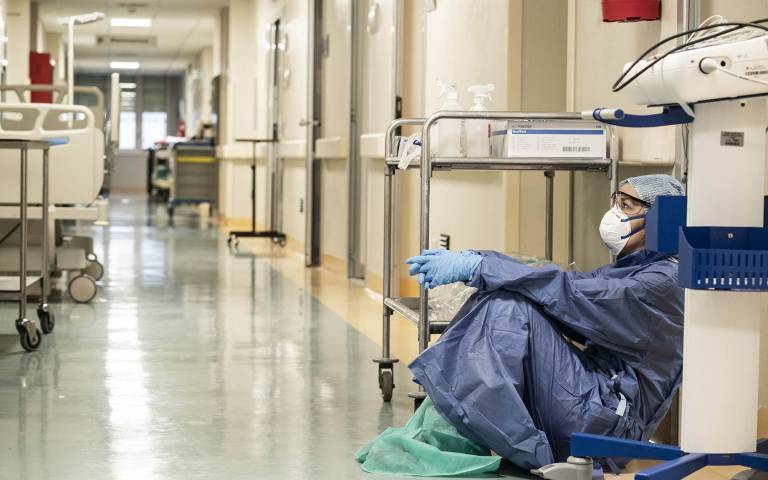 A doctor in PPE rests on the floor of a hospital