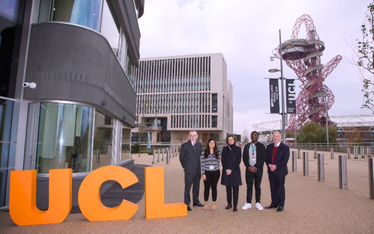 UCL staff and students outside the One Pool Street Campus on the university's new UCL East campus, with a UCL flag and its Marshgate building, the ArcelorMittal Orbit sculpture and London Stadium in the background