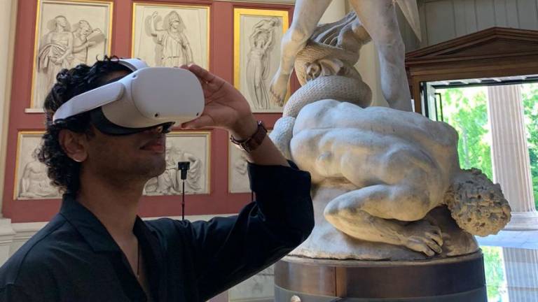 Man wearing a VR headset in a museum with sculptures behind him