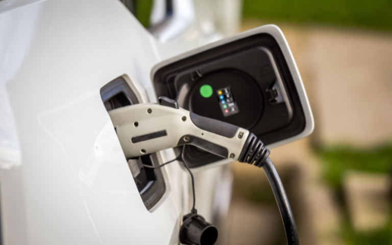 A close-up of an electric vehicle charging, showing the charging lead plugged in to the side of the car