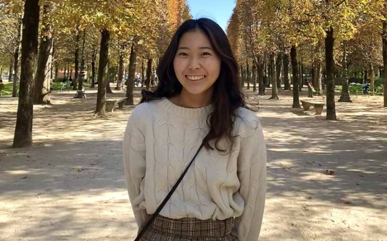 UCL student Haruna Doi. She is smiling, standing outside on a tree-lined avenue in a park.