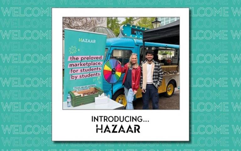 Two students stand by a stall with a banner with the text 'Hazaar: the preloved markeplace for students, by students'.
