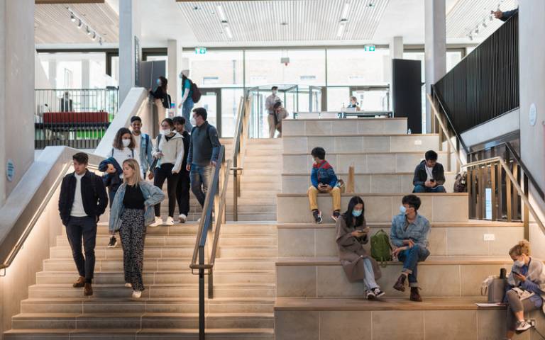 students are walking and sitting on the side stairs inside the bright UCL Student Centre