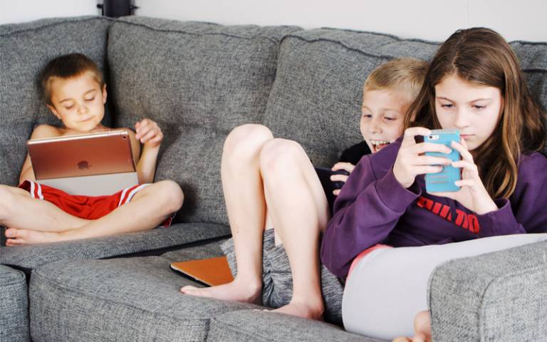 Children lying on sofa and using gadgets