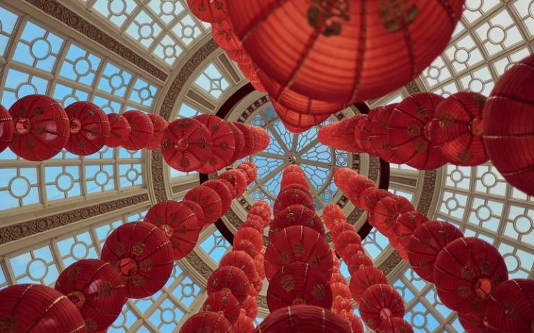 Strings of red and gold lanterns hanging from an ornate ceiling, seen from below