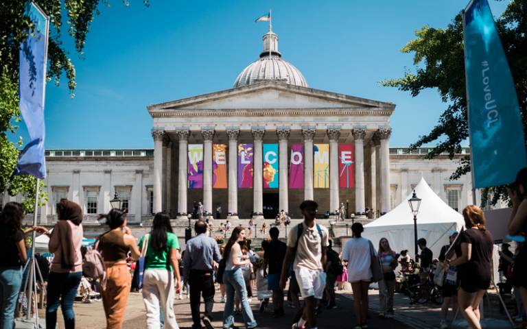 A crowd of people in the Quad at UCL's 2022 Open Days. The sky is blue and the Portico is displaying banners that say "welcome".