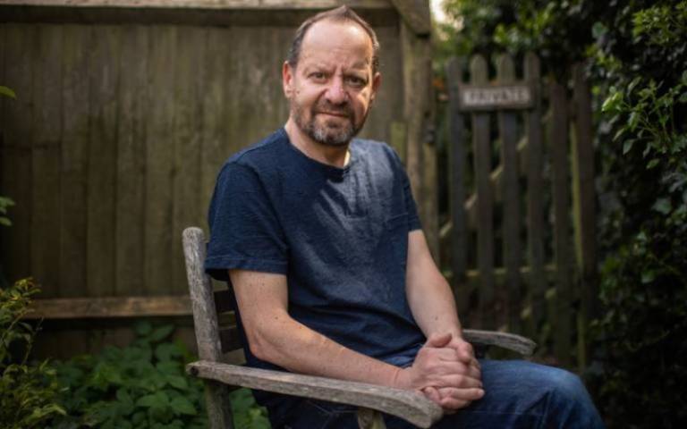 Philippe Sands sits on a wooden chair in a garden