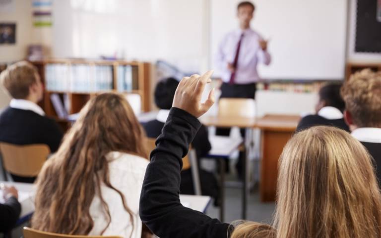 Image shows a student raising her hand in class