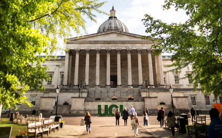 View of the UCL Quad in the sunshine, with people walking around and large 3D letters 'UCL' standing near to the Portico building