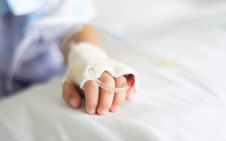 A child's hand on a hospital bed with intravenous drip attached