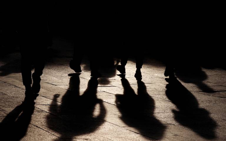 A group of obscured individuals walk down a shadowy street