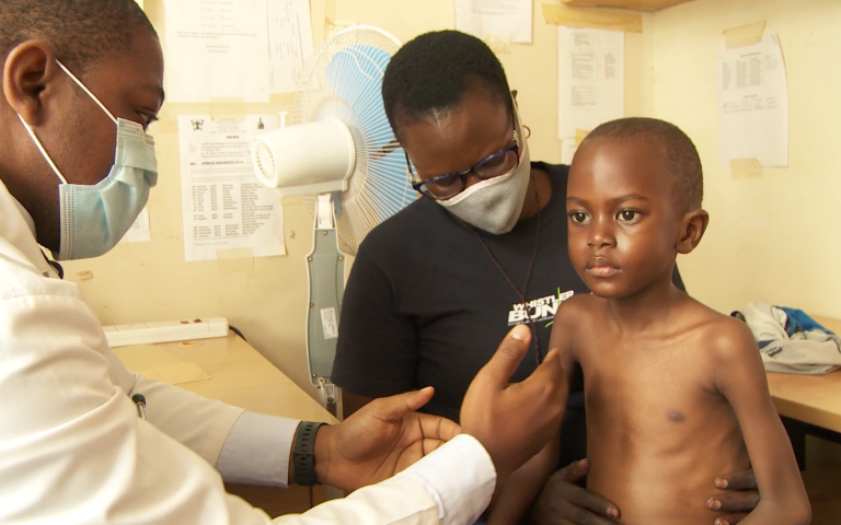 One of the children involved in the SHINE trial sits on his mother's lap while a doctor examines his chest