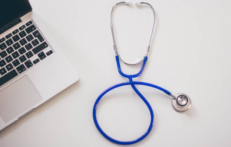 An image of a stethoscope lying on a surface next to a laptop.