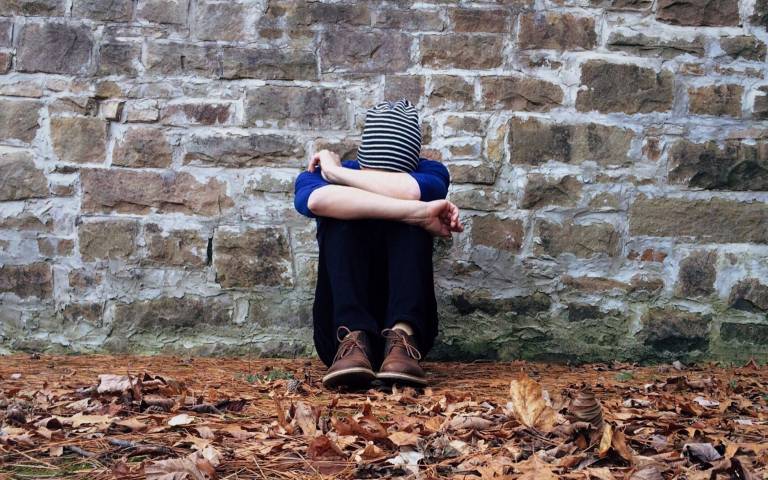 boy leaning against wall with knees hiding face