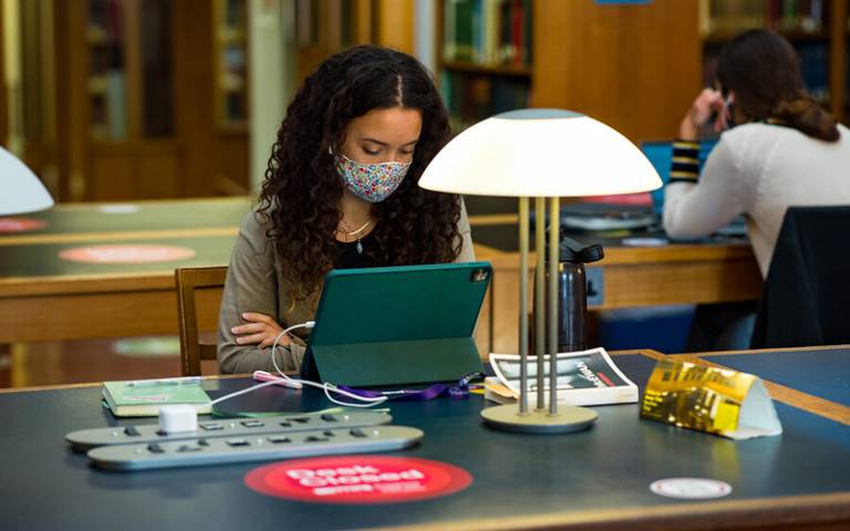 A student wearing a face covering, working in the UCL Library