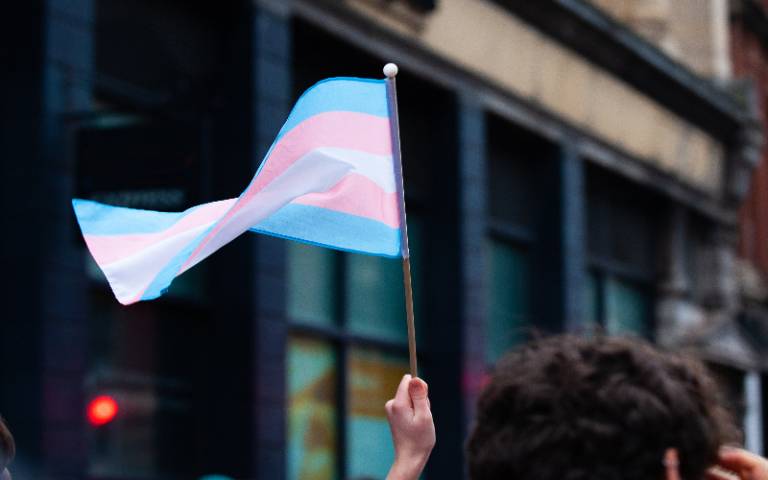 A hand holds up a small transgender pride flag in a Bristol Street. The transgender pride flag is a symbol of pride for the trans community. 