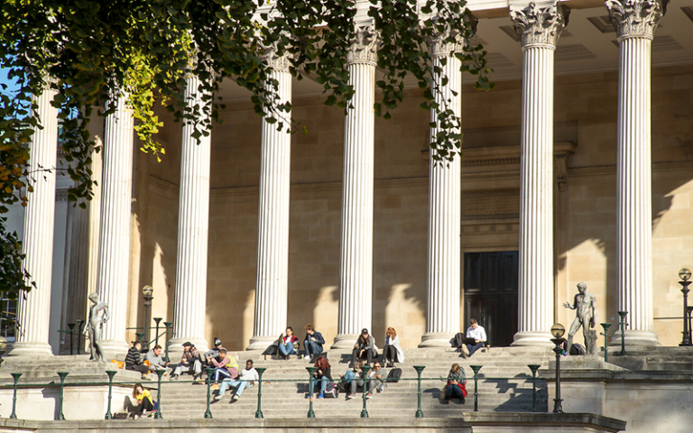 The UCL portico building with students sitting on the steps
