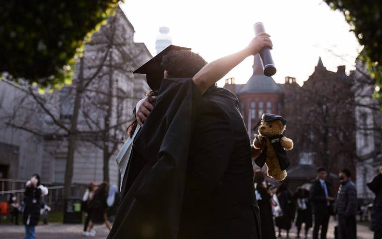 Two UCL graduates in gowns hugging each other