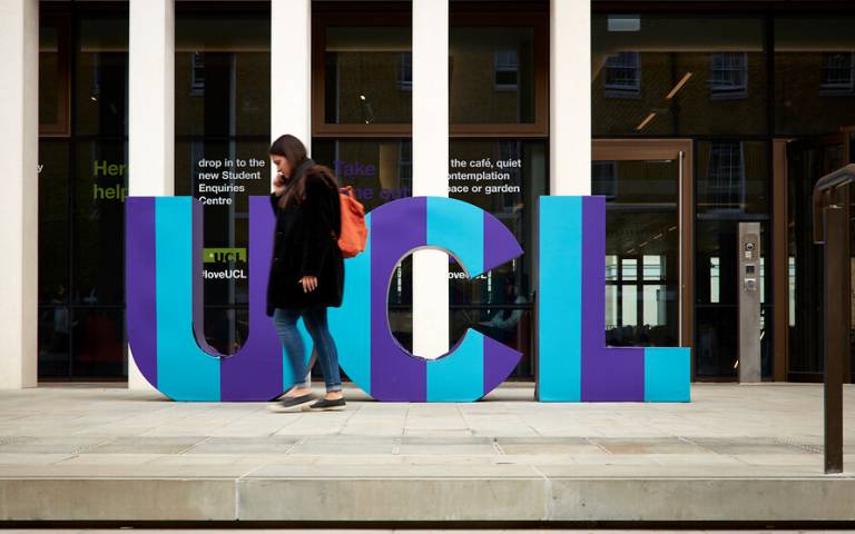 A female student walks in front of a UCL sign