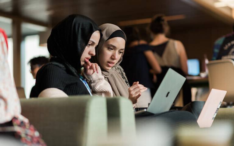 Two students sit working on their laptop