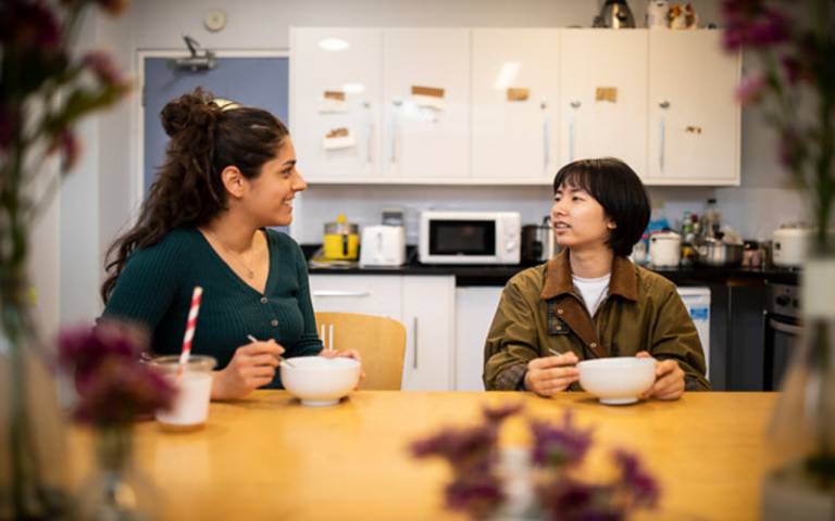 two students sit in their halls accomodation kitchen and eat and chat