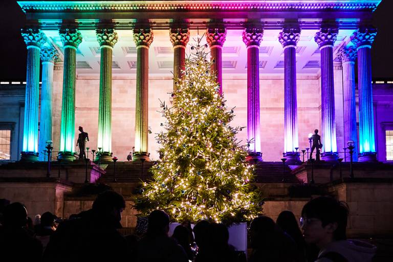 Festive lights on UCL's Portico, Christmas 2022. There is an illuminated Christmas tree against the portico pillars lit up in rainbow colours.