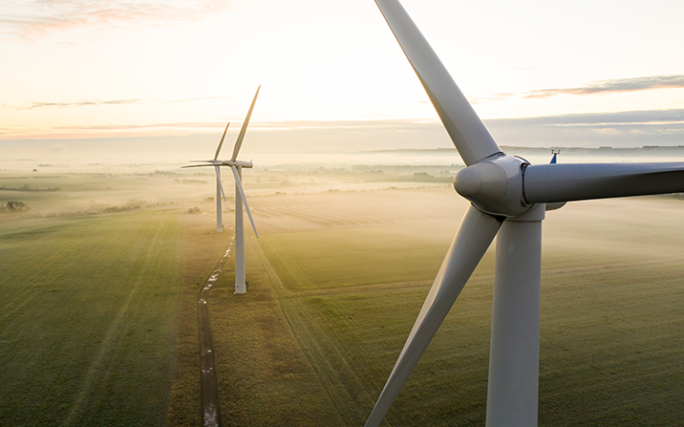 Aerial view of three wind turbines in the early morning fog at sunrise in the English countryside
