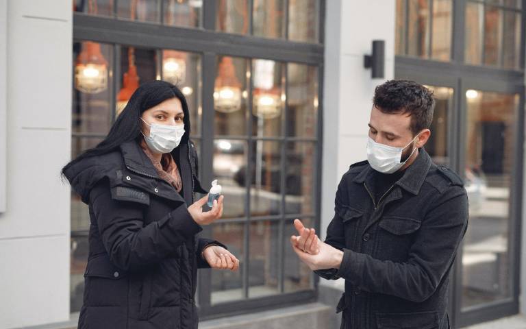 young couple in face masks using hand gel