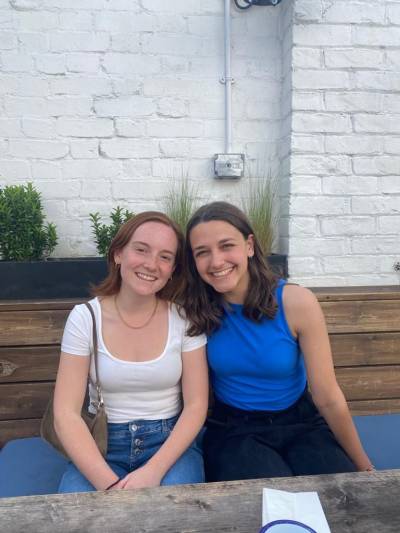 two women smile towards the camera from wooden bench seating