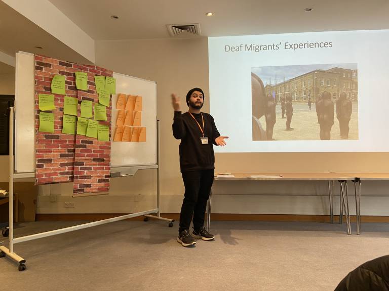 man talking in front of deaf migrants experiences presentation slide