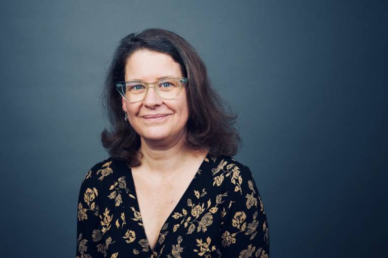 Prof. Kearsy Cormier wearing a flowery top and positioned in front of a dark blue background