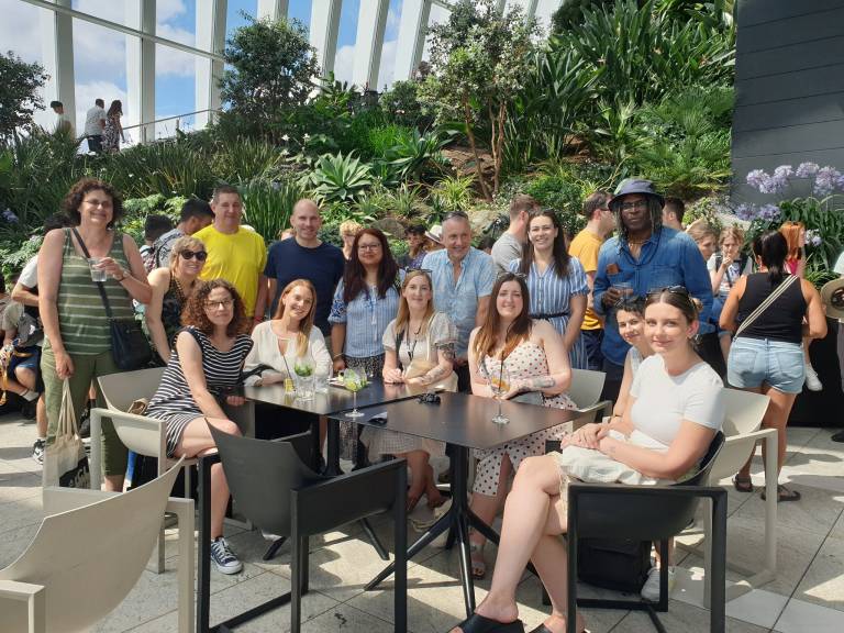 A group of PALS Professional Services Staff are gathered around a table in front of a large section of the garden at London's Sky Garden