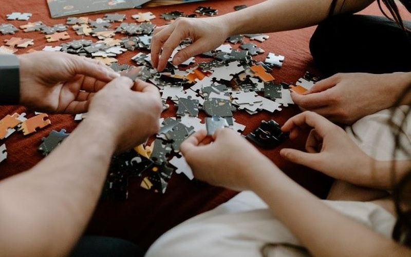 Image of people completing a jigsaw puzzle, no faces visible, image only shows their arms and hands