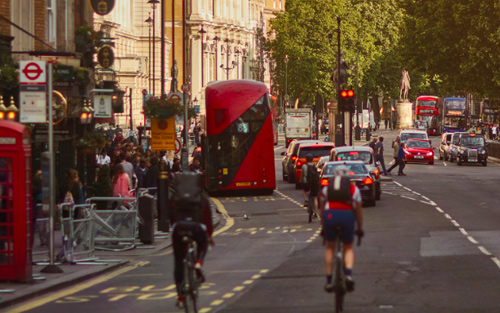 Two cyclists riding their bikes through London, with a bus in the background