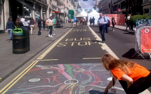 A young woman in an orange shirt painting chalk designs on a London street