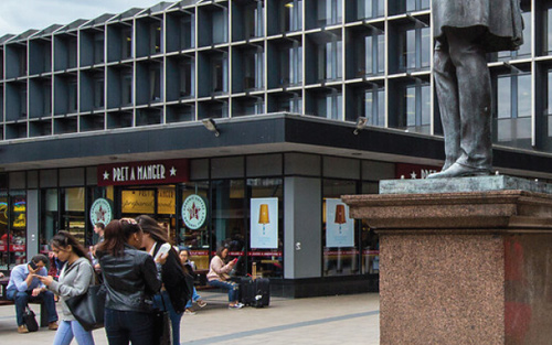 Part of a statue in Euston, with some office blocks and a cafe behind it