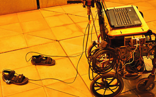 A pair of shoes attached to a wheelchair with a computer sitting on it, linked by some wires