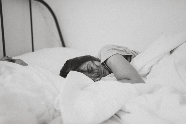 A person sleeping. They are covered by a white linen duvet. 
