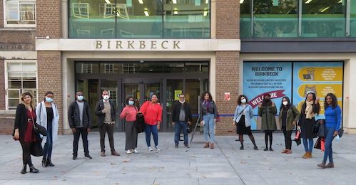 Diverse group of students with masks standing in a socially-distanced semi-circle near the entrance to one of Birkbeck University's buildings