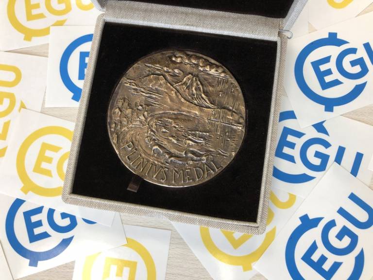 EGU award medal in presentation box surrounded by EGU logos in blue and yellow 