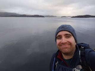 Dr Joel Davis smiling at the camera in front of a lake